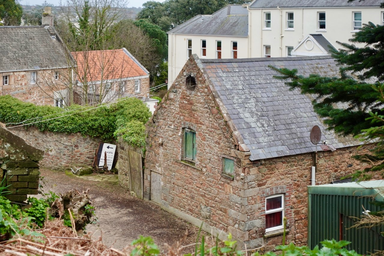 Jersey granite outhouse at La Haule, St Brelade, with deteriorated wood doors and windows in need of a 3rd-Party condition report for renovation.